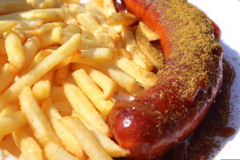 Traditional German Currywurst served with crispy chips, covered in rich curry ketchup and curry powder – the classic German street food favourite now available in the UK.
